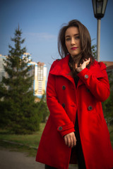 Beautiful girl in a red coat on a background of trees