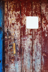 Closeup image of red wooden rusty door with white blank plate. 