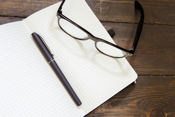 Reading glasses and notepad on wooden background