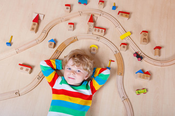 Little blond child playing with wooden railroad indoor