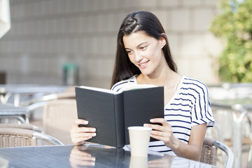 Smiling woman reads book in the terrace restaurant.