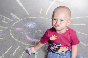 Naklejka premium little boy draws with chalk on the pavement sun