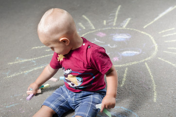 Naklejka premium little boy draws with chalk on the pavement sun
