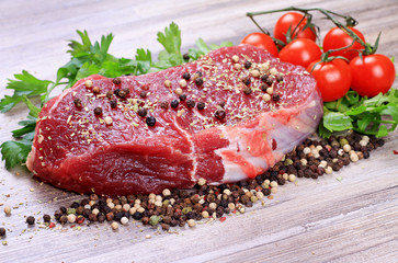 Raw beefsteak with spices and cherry tomatoes on wooden background