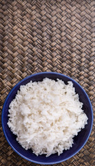 Cooked steamed rice in a blue bowl over wicker background