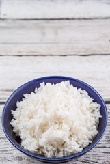 Cooked steamed rice in a blue bowl over wooden background