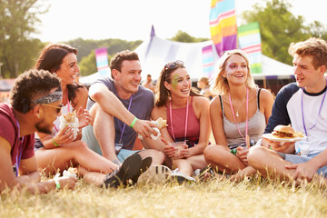Friends sitting on grass and eating at music festival
