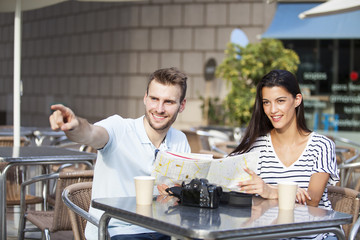 Happy couple tourists consulting a guide in a restaurant terrace. Vacation concept
