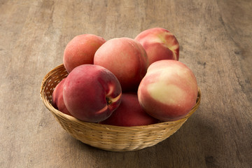 Some peaches in a basket over a wooden surface