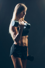 Athletic woman with dumbbells on a dark background