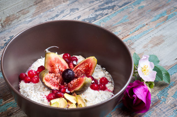 Home made bircher style muesli porridge topped with fresh sliced fig, pomegranate seeds, pistachio nuts coconut,chia seeds and a cherry. Served on a rustic wooden table.