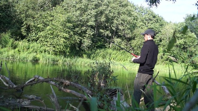 Fisherman catches spinning throws the bait downstream and then bandaging tackle. The action takes place on a small river in the summer morning near the forest. Video with sound.