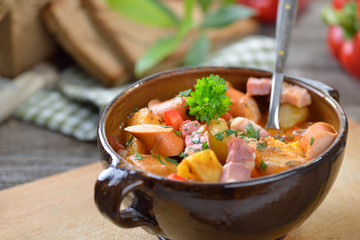 Kräftiges Kartoffelgulasch mit Speck und Wiener Würstchen in der Keramikschale
