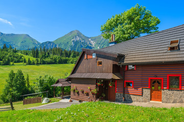 Typical wooden house on green meadow with Tatry Bielskie Mountains in background in summer, Slovakia