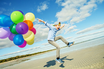Happy boy plays with colored balloons on the beach