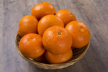 Some tangerines in a basket over a wooden surface