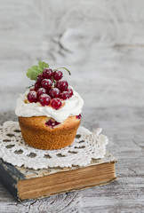 cupcake with cream and red currants and a book on a light wooden background, vintage style