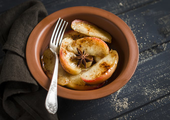 caramelized apples with cinnamon and honey in a clay dish on dark wooden background