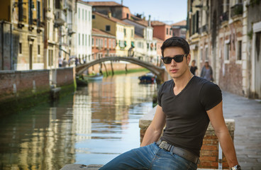 Fototapeta na wymiar Young Man on Bridge Over Narrow Canal in Venice