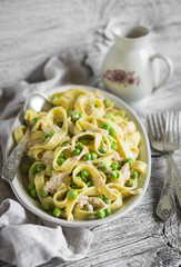 homemade pasta with chicken, green peas and cream sauce on an oval plate on a light wooden background