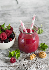 berry smoothie in a glass jar and berries in a white bowl on a light wooden background, healthy snack