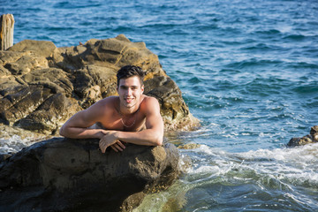 Young shirtless athletic man leaning on rock by sea