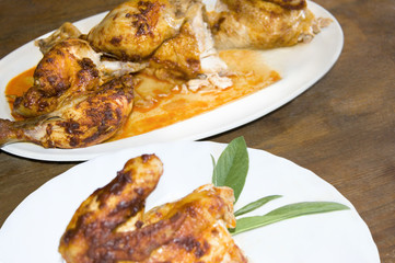 Quarter of roast chicken with red pepper crust and a sprig of sage on a white porcelain plate.