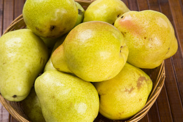 Some pears in a basket over a wooden surface seen from above