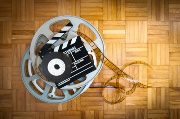 Movie clapper board and film reel on wooden floor