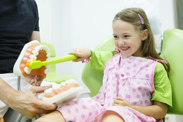 Girl in dentists chair toothbrushing a model - 87491952