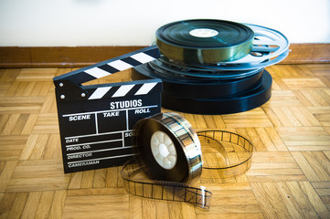 Movie clapper board and film reel on wooden floor