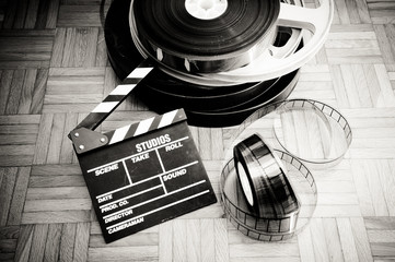 Movie clapper board and film reel on wooden floor
