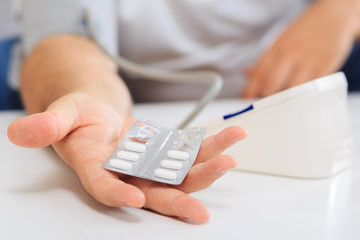 Male hand  holding medication and measuring blood pressure