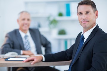 Confident businessman looking at camera with colleague behind 