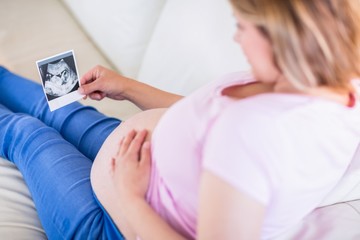 Pregnant woman looking at ultrasound scans and touching belly