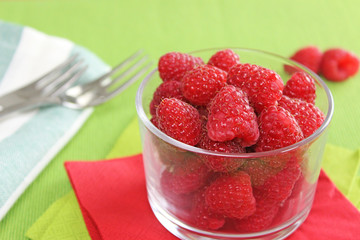 Himbeeren in Schale aus Glas mit grüner Serviette und Besteck - Beeren naschen