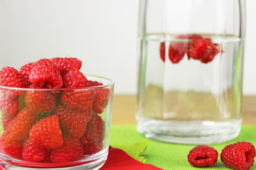 Himbeeren in Schälchen in in Karaffe mit Wasser auf Tisch