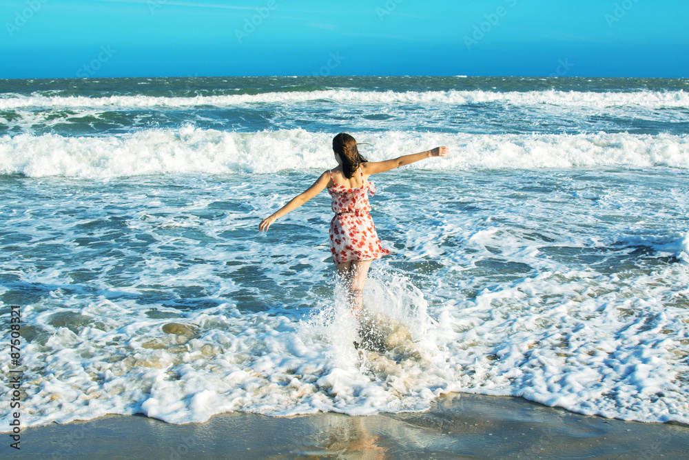 Wall mural woman running in waves of an ocean at the beach