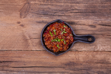 Mince meat ragu with chopped herbs on shot in a rustic old vintage pot on a wooden background from above