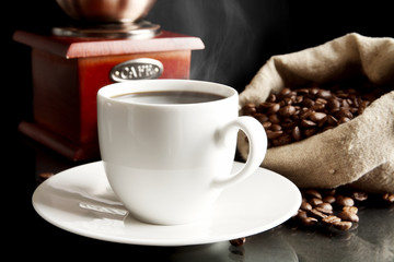 Cup of coffee with mill,bag full of coffee beans on black