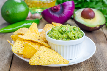Cup with chunky guacamole served with nachos and ingredients on backgroung