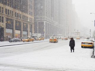 Man walking in a city in the snow during a blizzard, yellow taxis on the street.