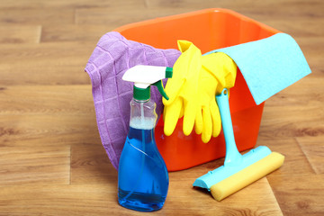 Tools needed for cleaning house in the orange bucket on a brown wooden floor