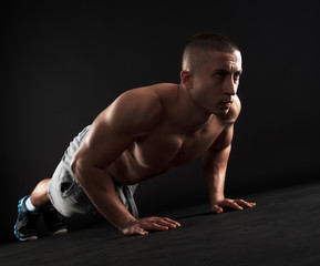 Young fitness man doing push-ups on floor, isolated on black background