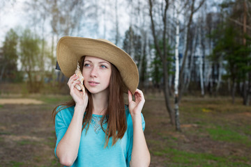 Freckled girl in hat listening to shell
