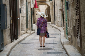 Turista con cappello e borsetta in una vecchia strada di paese