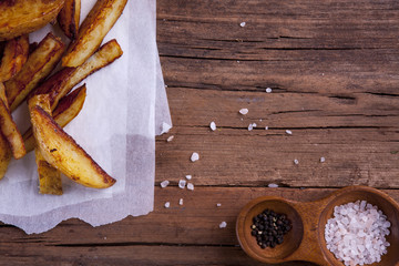 Wedges shot on a wooden background from above with salt and pepper and on cooking or greaseproof paper with negative space