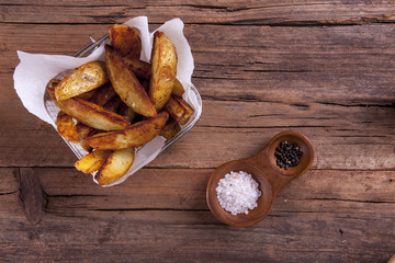 Wedges shot on a wooden background from above with salt and pepper and in a basket on cooking or greaseproof paper
