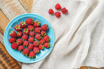 Red rasberry in blue dish and in front of white fabric on old vi
