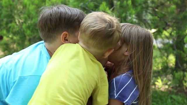 Mother with three children, two boys and girl, children hug and kiss her
